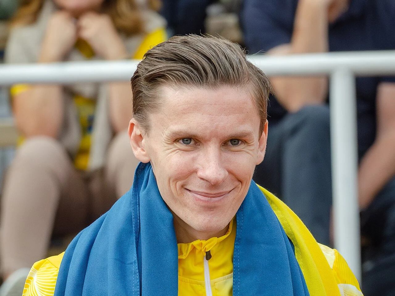 Andreas Almgren ler med en svensk flagga över axlarna på en friidrottsarena