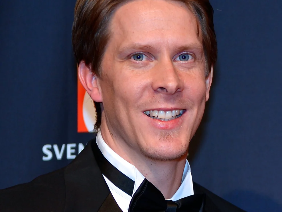 Christian Olsson i smoking och fluga ler mot kameran framför en mörkblå skylt på en svensk idrottsgala i januari 2014